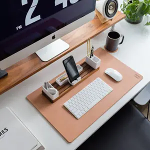 Desk with leather desk pad, walnut desk organizer, wireless keyboard and mouse, and porcelain mug.